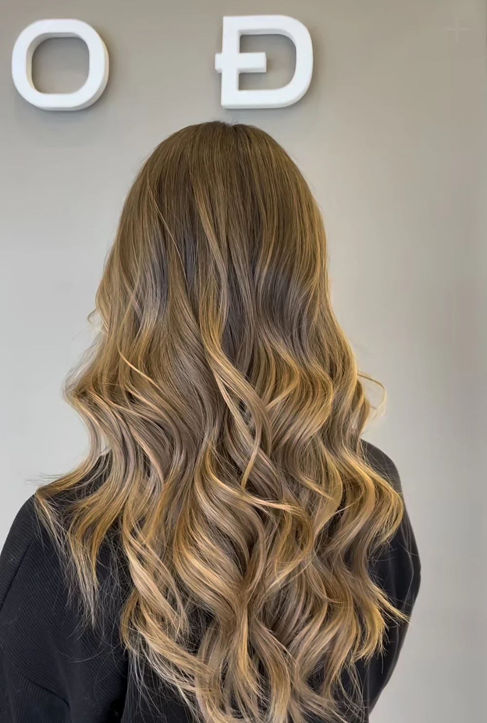 Pelo largo con iluminación y ondas frente al letrero de Estudio D